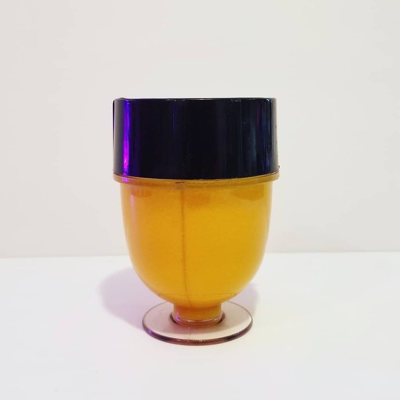 May include: A vintage-style, yellow plastic cup with a black lid. The cup has a rounded body and a clear, circular base. The cup is likely used for serving beverages or desserts. The background is plain white.