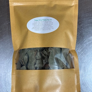 May include: A brown paper bag with a clear window, filled with dried green Sweet Sop leaves. The bag has a label with text that reads "Happy Being Nappy.etsy.com" and describes the product as a natural product from Kingston, Jamaica.