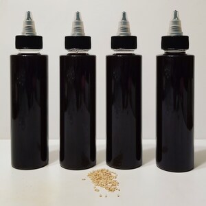 May include: Four black plastic bottles with clear tops and a small pile of sesame seeds in front of them.