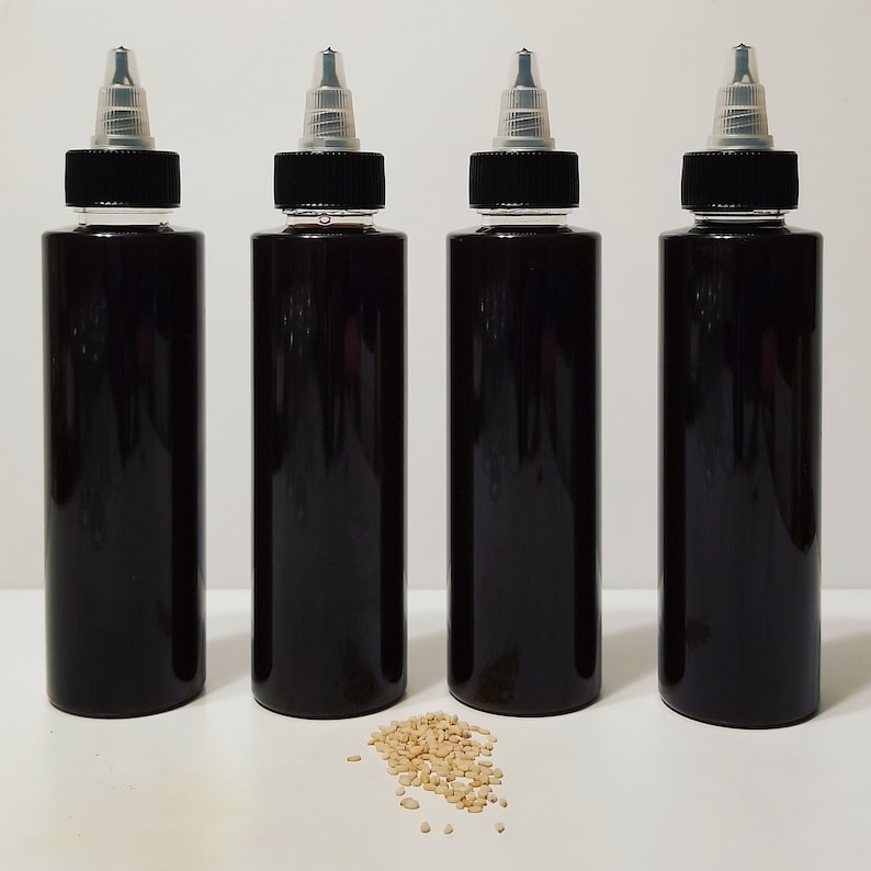 May include: Four black plastic bottles with clear tops and a small pile of sesame seeds in front of them.