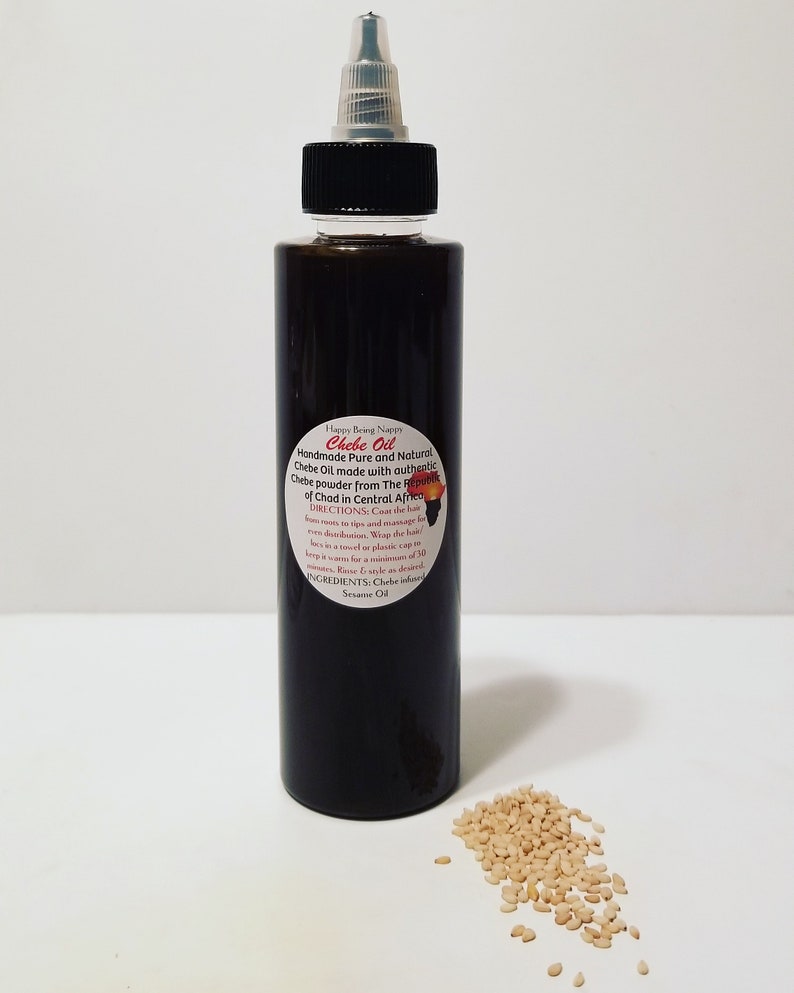 May include: A dark brown glass bottle with a black cap and a white label that reads "Chebe Oil Handmade Pure and Natural Chebe Oil made with authentic Chebe powder from The Republic of Chad in Central Africa". The bottle is sitting on a white surface with a small pile of light brown sesame seeds in front of it.