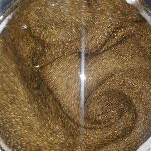 May include: A close-up of a pot filled with a swirling, shimmering, golden liquid. The liquid is thick and viscous, and it has a metallic sheen.