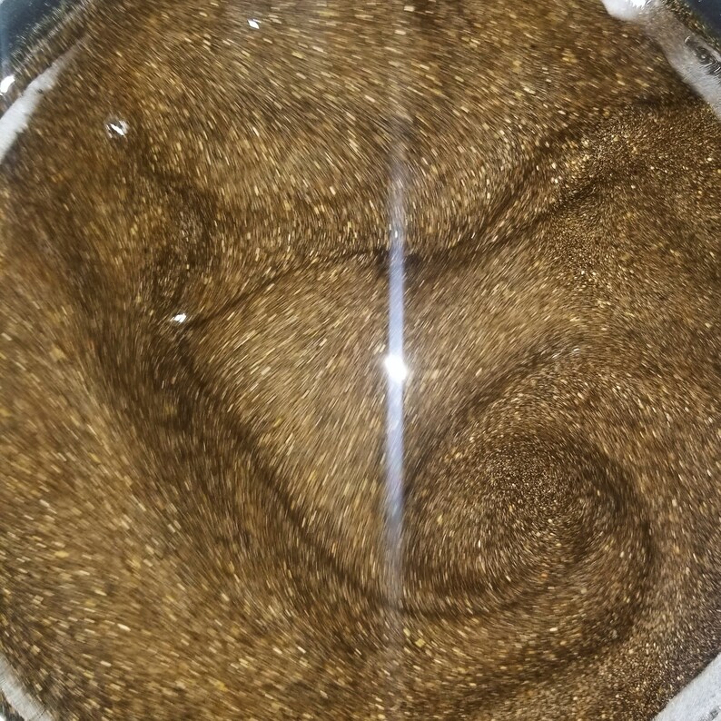 May include: A close-up of a pot filled with a swirling, shimmering, golden liquid. The liquid is thick and viscous, and it has a metallic sheen.