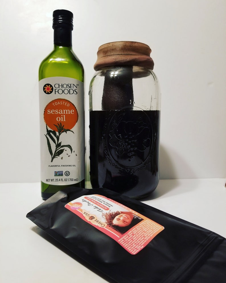May include: A glass jar with a brown lid filled with a dark liquid. A bottle of Chosen Foods Toasted Sesame Oil is next to the jar. A black pouch with a pink label that reads "Chebe USA Chebe Powder Authentic From Chad" is in the foreground.