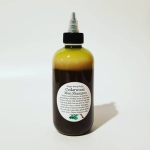 May include: A brown glass bottle with a green label that reads "Happy Being Nappy Cedarwood Men Shampoo". The label describes the shampoo as being great for promoting a healthy scalp and helping with dandruff and hair growth.