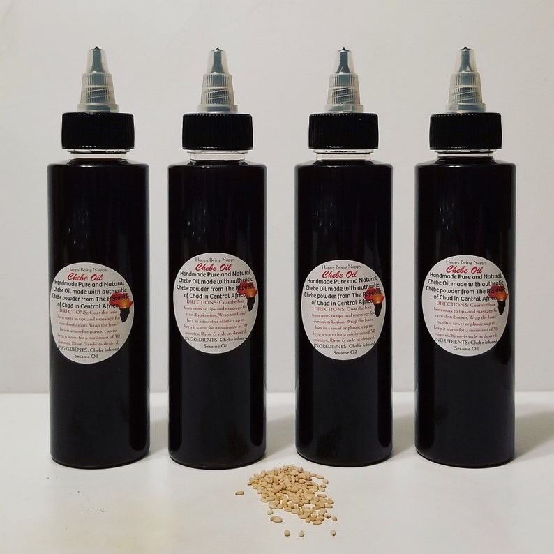 May include: Four dark brown glass bottles with black caps and labels that read "Chebe Oil Handmade Pure and Natural Chebe Oil made with authentic Chebe powder from The Republic of Chad in Central Africa". The bottles are arranged in a row on a white surface. A small pile of light brown seeds is in front of the bottles.