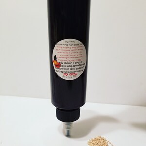 May include: A black bottle of Chebe Oil with a white label that reads "Chebe Oil Handmade Pure and Natural Chebe Oil made with authentic Chebe powder from The Republik DIRECTIONS Coathe hair Forestops and massage Prediaribution. Wrap the har locs in a towel or plastic cap to keep it was for a minimum of 30 mintes. Rise & style as desired. INGREDIENTS: Chebe infused. Sesame Oil". A small pile of sesame seeds is in the foreground.