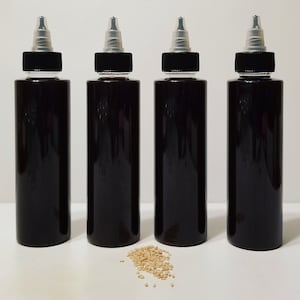 May include: Four black plastic bottles with clear caps and a small pile of sesame seeds in front of them.