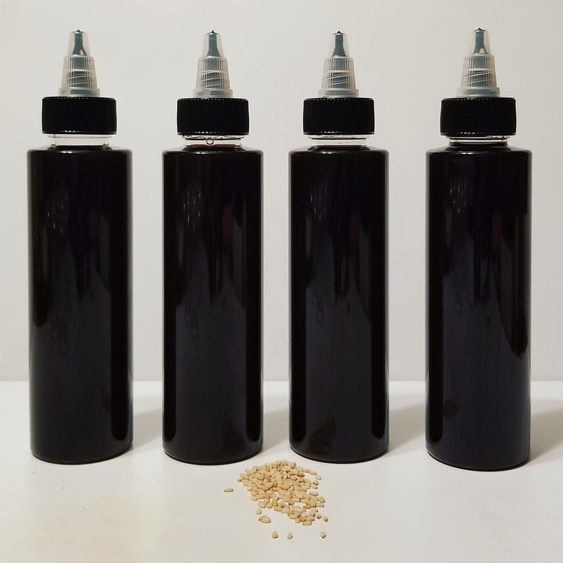 May include: Four black plastic bottles with clear caps and a small pile of sesame seeds in front of them.
