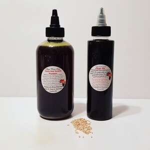 May include: Two glass bottles with dark liquid inside, labeled "Chebe Hair Growth Shampoo" and "Chebe Oil". The bottles have black caps and are sitting on a white surface with a small pile of light brown seeds in front of them.