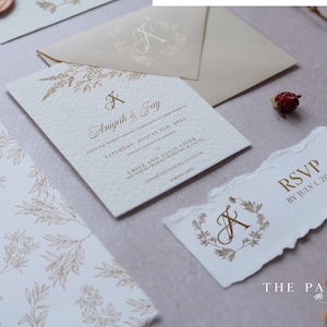 May include: A set of wedding invitations with a floral design and the names "Anjuah & Jay" printed on the front. The RSVP card has a torn edge and the text "RSVP by July 1, 2023".
