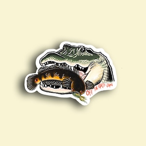 May include: A sticker featuring a cartoon illustration of an alligator with its mouth open, biting a fish. The text "OFF THE GRID JOHN" is printed on the sticker.