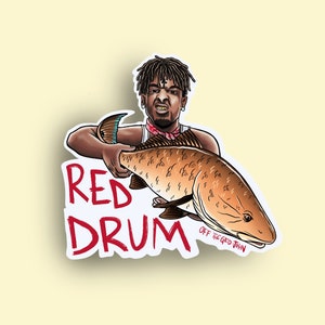 May include: A sticker featuring a cartoon illustration of a person holding a red drum fish. The text "RED DRUM" is in red letters and the text "OFF THE GRID JOHN" is in black letters.