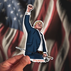 May include: A sticker of a cartoon man with a blue suit and red stripes on his face, holding a fishing rod with his right hand raised in the air. The sticker has the text "Off the Grid John" at the bottom.