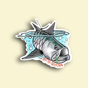 May include: A sticker featuring a cartoon illustration of a fish with a lure in its mouth. The fish is swimming in blue water with bubbles. The text "OFF THE GRID JOHN" is written below the fish.