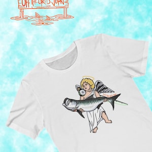 May include: White t-shirt with a graphic of an angel holding a fish. The angel has a halo and wings. The fish is a tarpon and has the text "Off the Grid John" on it.