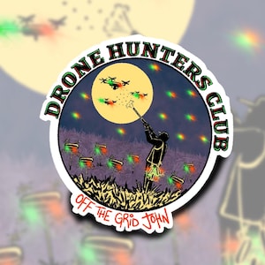 May include: A sticker with a dark blue background and a full moon. The moon has a yellow glow and a silhouette of a person aiming a rifle at a group of drones with red and green lights. The text "DRONE HUNTERS CLUB" is in a circle around the moon. The text "OFF THE GRID JOHN" is below the circle.