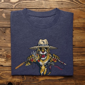 May include: A navy blue t-shirt with a cartoon illustration of a Florida panther wearing a hat and sunglasses, holding a fishing rod and a cigar. The text "Florida" is on the hat.