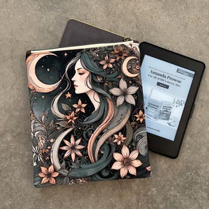 Puede incluir: Una funda decorativa con cremallera con un diseño celestial, que presenta el perfil de una mujer, flores y lunas en tonos de verde azulado, melocotón y crema. Junto a ella, un lector electrónico negro muestra texto de Amanda Prowse.