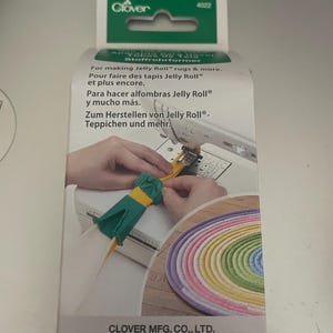 May include: A green and yellow plastic tool for making Jelly Roll rugs. The packaging shows a colorful rainbow rug and the text "For making Jelly Roll rugs & more. Pour faire des tapis Jelly Roll et plus encore. Para hacer alfombras Jelly Roll® y mucho más. Zum Herstellen von Jelly Roll®-Teppichen und mehr. CLOVER MFG. CO., LTD."
