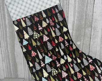 May include: A black Christmas stocking with a quilted design of colorful Christmas trees. The stocking has a blue and white plaid cuff.