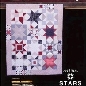 May include: A quilt with a star pattern in shades of red, white, and blue. The quilt measures 66" x 84". The design features various star shapes and geometric patterns. The text on the quilt says "Seeing Stars".