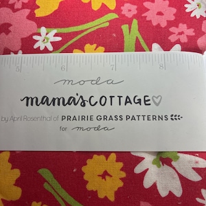 May include: Close-up of floral fabric with a ruler. The fabric is red with yellow, pink, and white flowers and green stems. The text "mama's COTTAGE" is visible, along with "by April Rosenthal of PRAIRIE GRASS PATTERNS for moda".