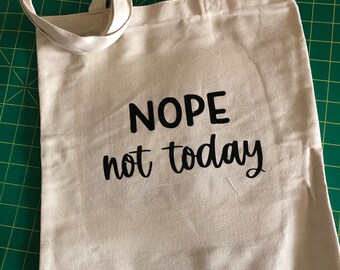 Könnte beinhalten: Beige Tragetasche mit schwarzem Text "NOPE not today". Die Tasche hat zwei Griffe und besteht aus einem leinwandartigen Material. Sie liegt auf einer grünen Oberfläche.