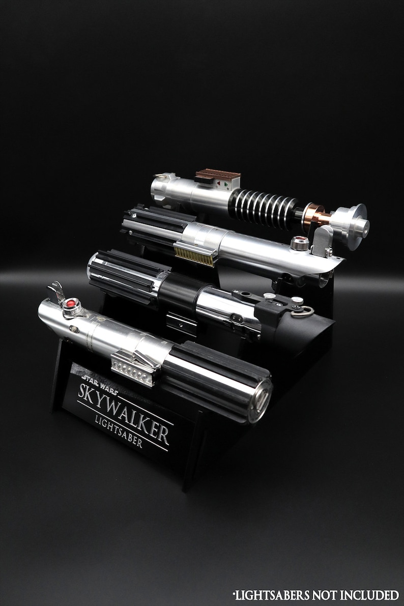May include: A black display stand with the text "Star Wars Skywalker Lightsaber" engraved on it. Four silver and black lightsabers are displayed on the stand. The text "Lightsabers not included" is at the bottom of the image.