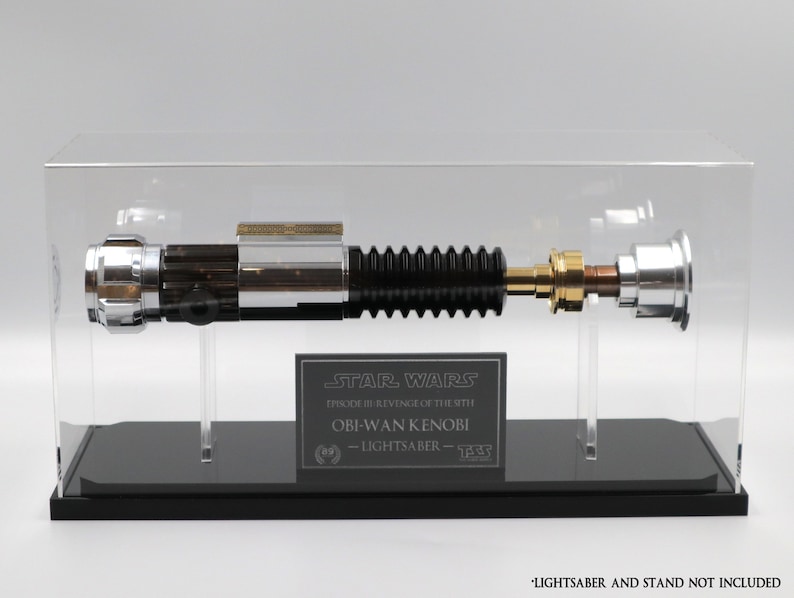 Puede incluir: Una r&eacute;plica de sable de luz negro y plateado de Star Wars Episodio III: La venganza de los Sith, expuesta en una vitrina de acr&iacute;lico transparente con una base negra. La vitrina presenta una placa con el texto "STAR WARS EPISODE III REVENGE OF THE SITH OBI-WAN KENOBI - LIGHTSABER - 833".