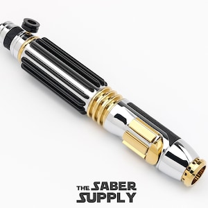 May include: A black and silver lightsaber with gold accents. The lightsaber has a black handle with silver accents and a gold ring around the middle. The lightsaber is on a white background.