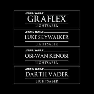 May include: Four white rectangular labels with black text on a black background. The labels are for Star Wars lightsabers. The labels read: Graflex Lightsaber, Luke Skywalker Lightsaber, Obi-Wan Kenobi Lightsaber, and Darth Vader Lightsaber.