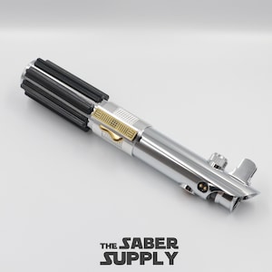 Könnte beinhalten: Ein silberner Lichtschwertgriff mit schwarzem Griff und goldenen Akzenten. Der Griff hat eine strukturierte Oberfläche und einen kleinen Knopf an der Seite.