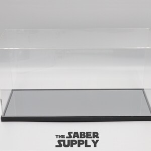 K&ouml;nnte beinhalten: Eine transparente Acryl-Vitrine mit schwarzem Sockel und einem grauen, verspiegelten Boden. Die Vitrine ist leer.