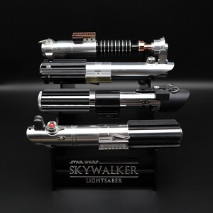 May include: A black stand with the text "STAR WARS SKYWALKER LIGHTSABER" displays four silver and black lightsaber replicas.