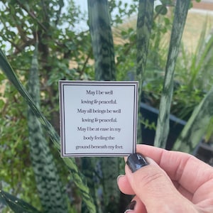 May include: A white card with black text that reads "May I be well loving & peaceful. May all beings be well loving & peaceful. May I be at ease in my body feeling the ground beneath my feet."