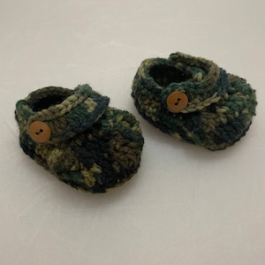 May include: A pair of green, brown, and black camouflage baby booties with brown buttons.