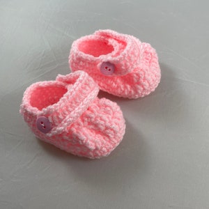 May include: A pair of pink crocheted baby booties with white buttons.