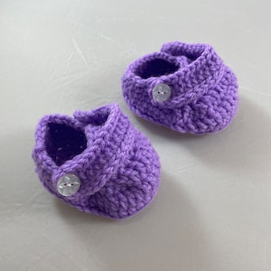 May include: A pair of purple crocheted baby booties with white buttons.