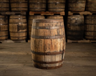 May include: A wooden barrel with metal bands, standing on a wooden floor. The barrel is made of weathered wood and has a rustic appearance. Other barrels are stacked in the background.