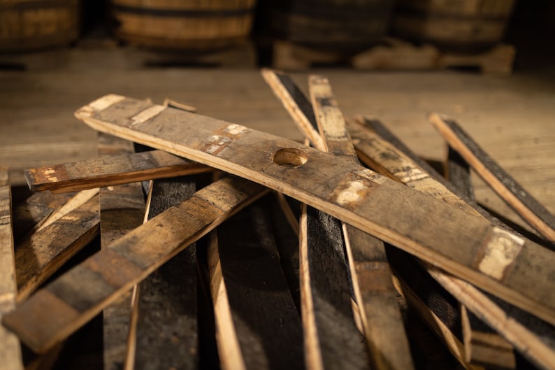 K&ouml;nnte beinhalten: Nahaufnahme von verwitterten Holzfassdauben, einige mit einem kleinen Loch, verstreut auf einer Holzoberfl&auml;che. Die Dauben sind in verschiedenen Braun- und Graut&ouml;nen gehalten, mit sichtbarer Holzmaserung und Textur. Der Hintergrund zeigt verschwommene Holzf&auml;sser.
