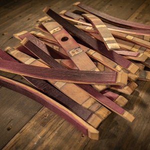 May include: A collection of reclaimed wood barrel staves, featuring a mix of colors including deep red, natural wood tones, and hints of purple. The staves are cut and shaped, with some showing metal hardware.