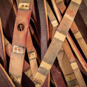 May include: Close-up of reclaimed wood barrel staves, showcasing varying shades of brown and red. Some staves have metal bands and a hole. The wood grain and textures are visible, creating a rustic aesthetic.