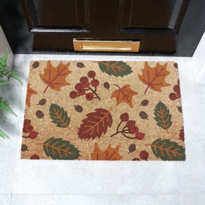 May include: A brown coir doormat with a autumn-themed design featuring red berries, orange, brown, and green leaves.