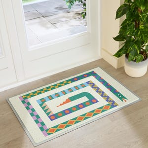 May include: A rectangular doormat with a cream-colored base featuring a stylized snake graphic. The snake is composed of geometric patterns in green, orange, blue, and purple, winding around the center with a visible head, eye, and tongue.