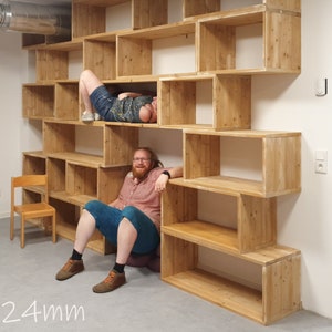 Puede incluir: Una estanter&iacute;a de madera con varios estantes de diferentes tama&ntilde;os. Los estantes est&aacute;n hechos de madera natural y tienen un aspecto r&uacute;stico. Dos personas est&aacute;n sentadas en los estantes, una est&aacute; tumbada y la otra est&aacute; sentada. Los estantes est&aacute;n contra una pared blanca.
