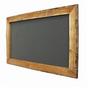 Puede incluir: Una pizarra rectangular con una superficie gris oscuro, enmarcada por un borde de madera marr&oacute;n claro r&uacute;stico. La madera tiene un aspecto natural, sin terminar, con vetas y textura visibles. La pizarra est&aacute; ligeramente inclinada.