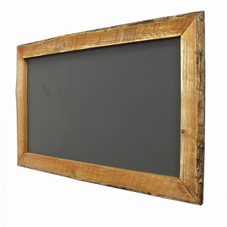Puede incluir: Una pizarra rectangular con una superficie gris oscuro, enmarcada por un borde de madera marr&oacute;n claro r&uacute;stico. La madera tiene un aspecto natural, sin terminar, con vetas y textura visibles. La pizarra est&aacute; ligeramente inclinada.