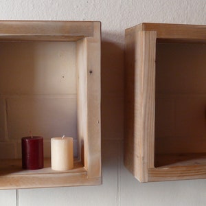 May include: Two wooden shelves with a rustic finish. The shelf on the left has a stack of books and two candles, one red and one white. The shelf on the right has a wooden heart.