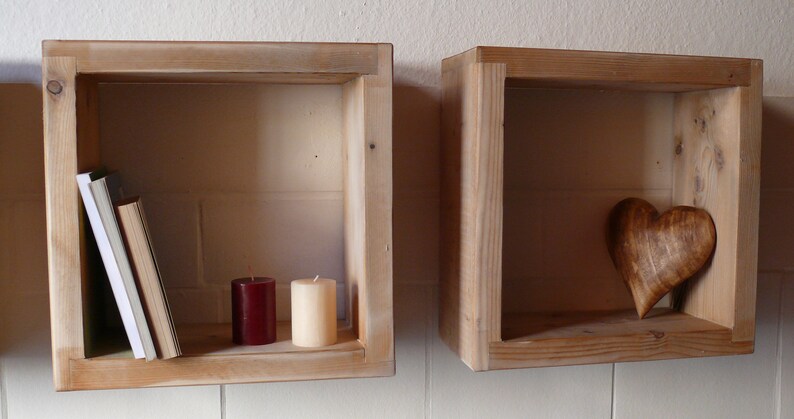 May include: Two wooden shelves with a rustic finish. The shelf on the left has a stack of books and two candles, one red and one white. The shelf on the right has a wooden heart.